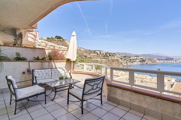 Un balcon agrémenté de mobilier d’extérieur, avec vue sur la mer et une colline en arrière-plan.