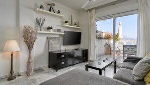 A modern living room with a flat-screen TV, a sofa, a coffee table, and a dining area with a table and chairs.