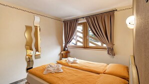 Ein Zimmer mit zwei Betten, einem Spiegel, einem Fenster mit Vorhängen und einer Wandleuchte.