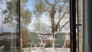 A view through a glass door of a patio area with two green chairs, a stone wall, and a large tree. - 'Lavanda' Apartment with Sea View, Garden, and Wi-Fi (Finale Ligure)