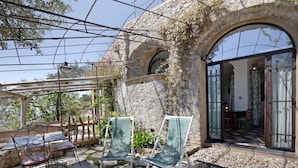 An outdoor seating area with chairs and tables, a stone wall, and a view into a room with a tiled floor. - 'Lavanda' Apartment with Sea View, Garden, and Wi-Fi (Finale Ligure)