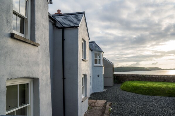 A row of white buildings with grey roofs, a gravel path, and a grassy area. - Brook Cottage Green - 2 Bedroom - Dale (Haverfordwest)