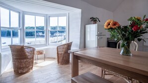 Eine helle Küche mit einem großen Fenster, Korbstühlen, einem Holztisch und einer Blumenvase.