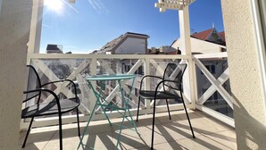 A balcony with a glass table and two chairs, a white pergola, and a view of buildings and a clear sky. - Bright city-center apartment for 4 people (Arcachon)
