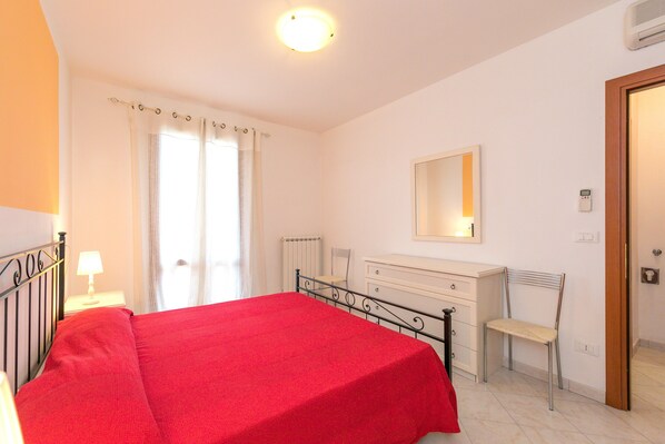 Une chambre à coucher avec un lit, une table de chevet avec une lampe, une commode, une chaise, un miroir et une porte.