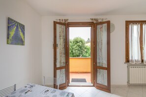 Une pièce comprenant une table à manger, un radiateur et donnant sur un balcon avec un arbre.