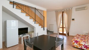 A modern kitchen with a refrigerator, a dining table with chairs, a TV, and a staircase. - Apartment 'Bilocale Correggiolo' with Terrace, Shared Pool & Wi-Fi (Suvereto)