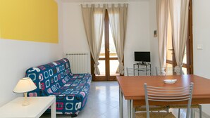 Ein Zimmer mit einem Bett, einem Tisch, Stühlen, einem Fernseher und Vorhängen.