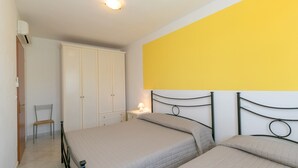 Ein Schlafzimmer mit zwei Betten, einem Sessel, einem Kleiderschrank und einem Nachttisch mit Lampe.