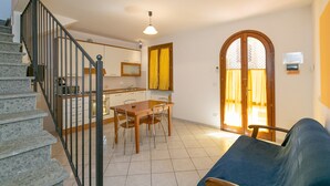 Una scala conduce a una cucina con tavolo e sedie, un divano e un'ampia finestra ad arco.