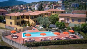 A pool area with lounge chairs and umbrellas, surrounded by buildings with red-tiled roofs. - Apartment 'Bilocale Ansonica' with Balcony, Shared Pool & Wi-Fi (Suvereto)