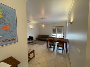 Un salon comprenant une table à manger, des chaises, un canapé, une carte accrochée au mur et une fenêtre avec des stores.
