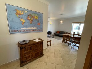 A living room with a world map, a wooden cabinet, a dining area with chairs, a sofa, and a TV.