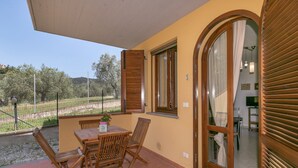 A balcony with a table and chairs, a view of the countryside, and a door leading to an interior space.