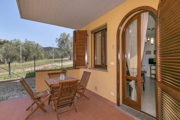 A balcony with a table and chairs, a view of the countryside, and a door leading to an interior space.