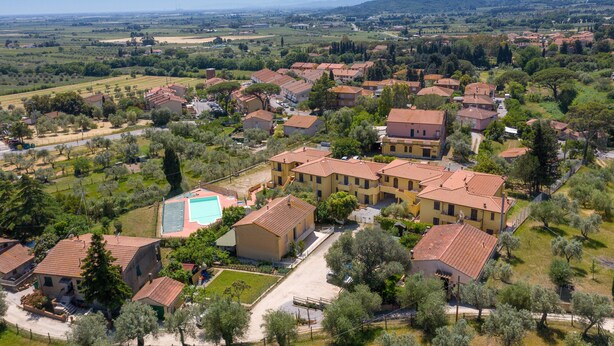 An aerial view of a residential area with houses, a swimming pool, and surrounding greenery.