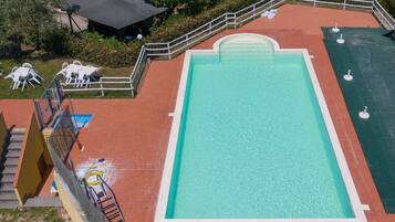 Une piscine rectangulaire bordée de blanc, entourée d’une zone pavée de briques rouges et d’une rambarde blanche.