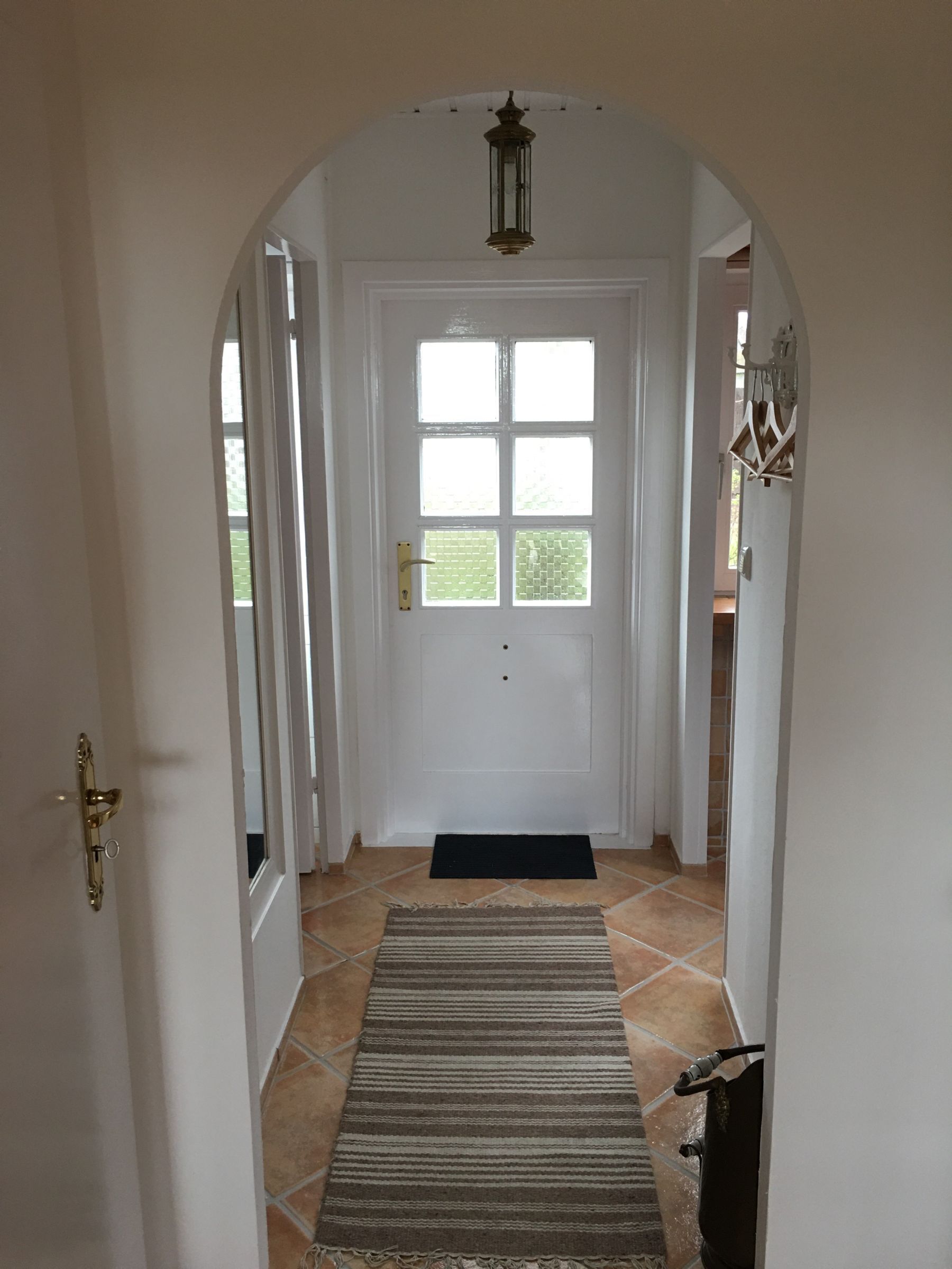 A hallway with a white door, a black doormat, and a striped rug.
