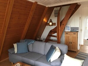 Ein gemütliches Loftsesselzimmer mit grauem Sofa, Holzbalken, einer Treppe und einem Holzschrank.