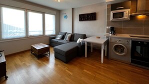 A modern apartment with a grey sofa, a small table, a washing machine, and a microwave.