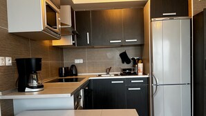 A modern kitchen with dark cabinets, a stainless steel refrigerator, a coffee maker, and a sink.