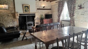 A rustic room with exposed beams, a stone fireplace, leather seating, and a dining table. - Charming Riverside Cottage with Private Grounds, Fishing, Pet-Friendly, WiFi, and Parking (Mareuil-sur-Arnon)