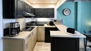 A modern kitchen with dark cabinets, a wooden countertop, a coffee maker, a toaster, and a clock on the wall. - Cozy 1BR Apartment in Mont-Dore Center, Near Thermes & Amenities, Sleeps 4 (Mont-Dore)