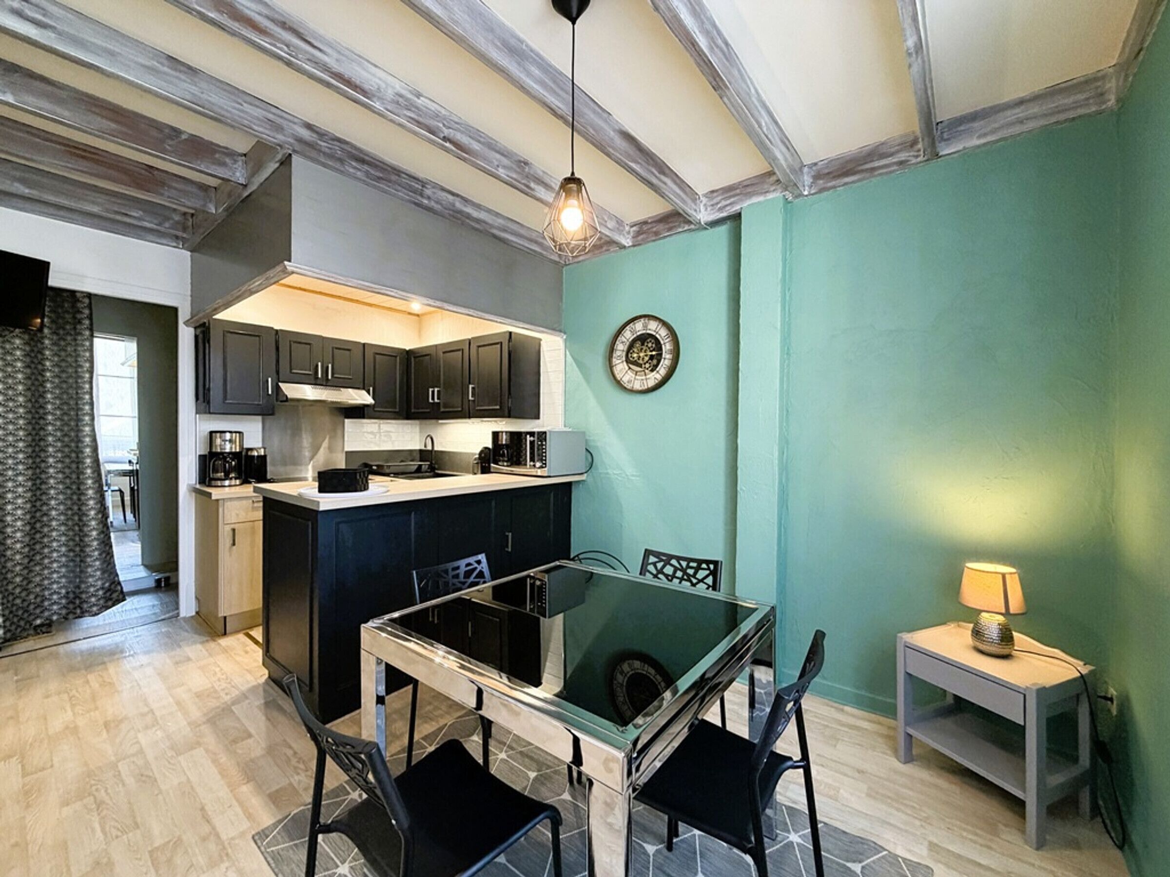 A modern kitchen with dark cabinets, a glass dining table, and a small side table with a lamp.