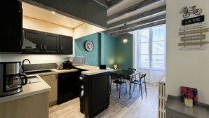 A modern kitchen with dark cabinets, a coffee machine, and a dining area with a table and chairs. - Cozy 1BR Apartment in Mont-Dore Center, Near Thermes & Amenities, Sleeps 4 (Mont-Dore)
