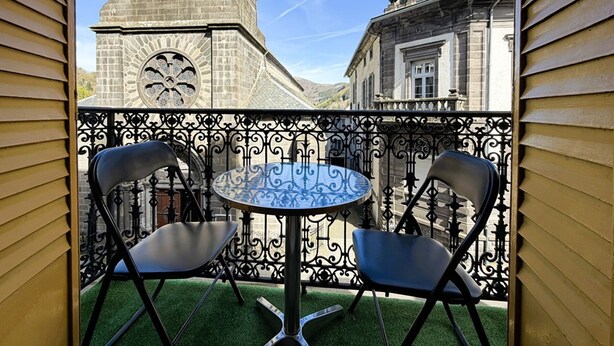 A balcony with a wrought iron railing, two chairs, and a round table. - Cozy 1BR Apartment in Mont-Dore Center, Near Thermes & Amenities, Sleeps 4 (Mont-Dore)