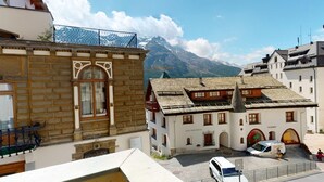 A traditional European building with a stone facade, a balcony with metal railings, and a mountain backdrop. - In the heart of St. (St. Moritz)