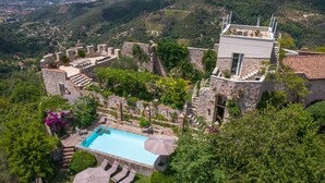 A high-altitude view of a historic stone building with a swimming pool, outdoor seating, and lush greenery. - Villa with heated pool and amazing view, Camaiore (Camaiore)