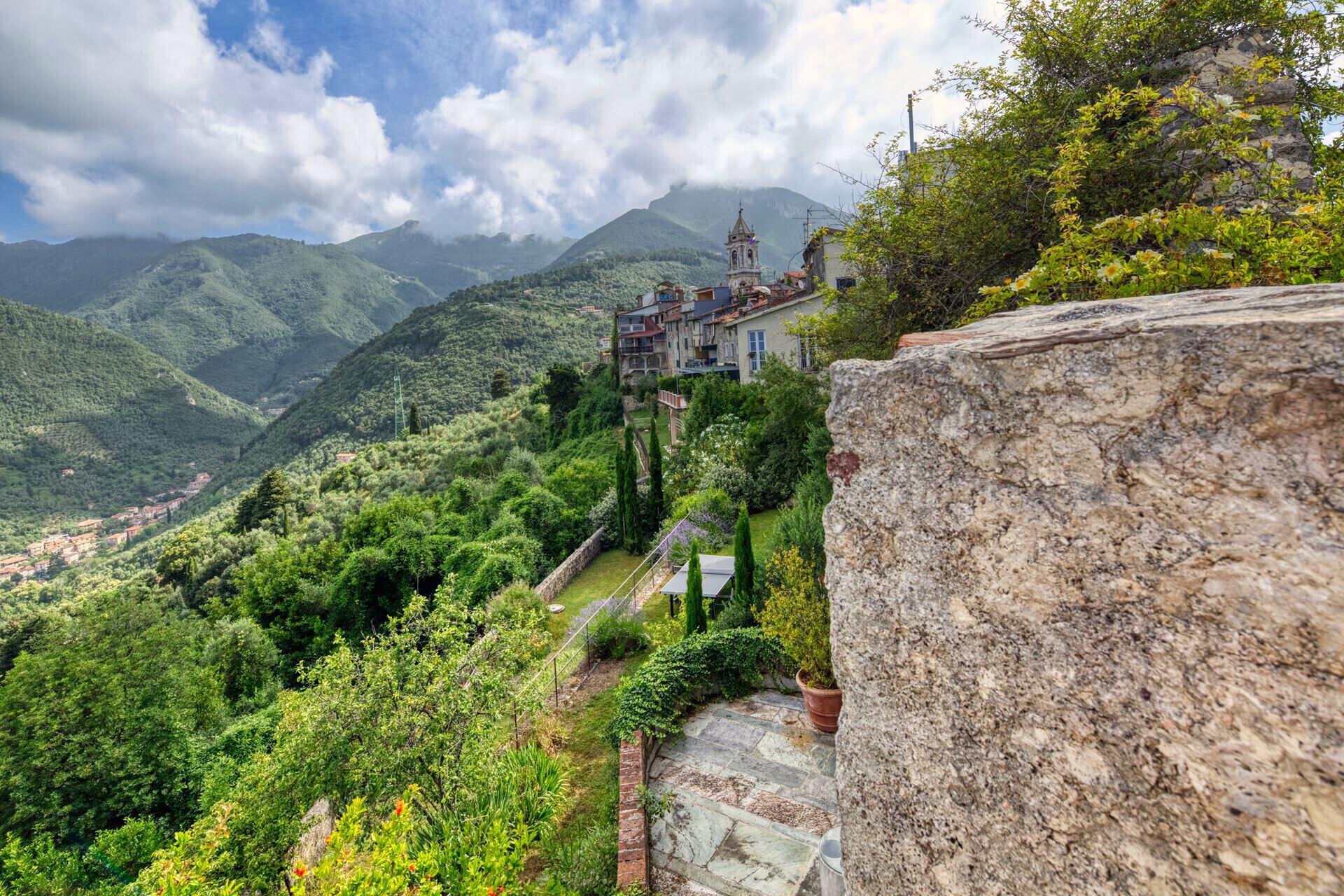Un village de montagne avec une église imposante située sur une colline, entouré d’une végétation luxuriante et d’un mur de pierre.