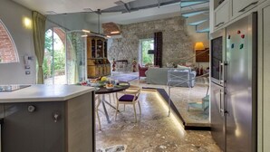 A modern kitchen with a stone wall, a dining area with a table and chairs, and a built-in refrigerator. - Villa with heated pool and amazing view, Camaiore (Camaiore)
