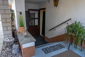 A stone bench, a potted plant, a door with a lace curtain, and a metal handrail.