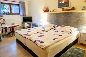 A double bed with floral bedding, a wooden nightstand, a lamp, a television, a window with curtains, and a shelf with decorative items. - Timmy Vacation Apartment - Vacation Apartment (Lubmin)