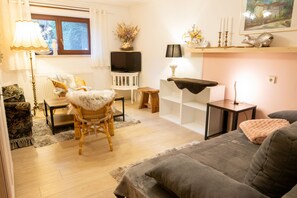 A living room with a sofa, a chair, a television, a lamp, and a shelf with decorative items. - Timmy Vacation Apartment - Vacation Apartment (Lubmin)