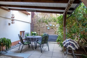A patio with a table and chairs, a hanging wind chime, and a wooden fence with climbing plants. - Vacation apartment Timmy - Holiday apartment (Lubmin)