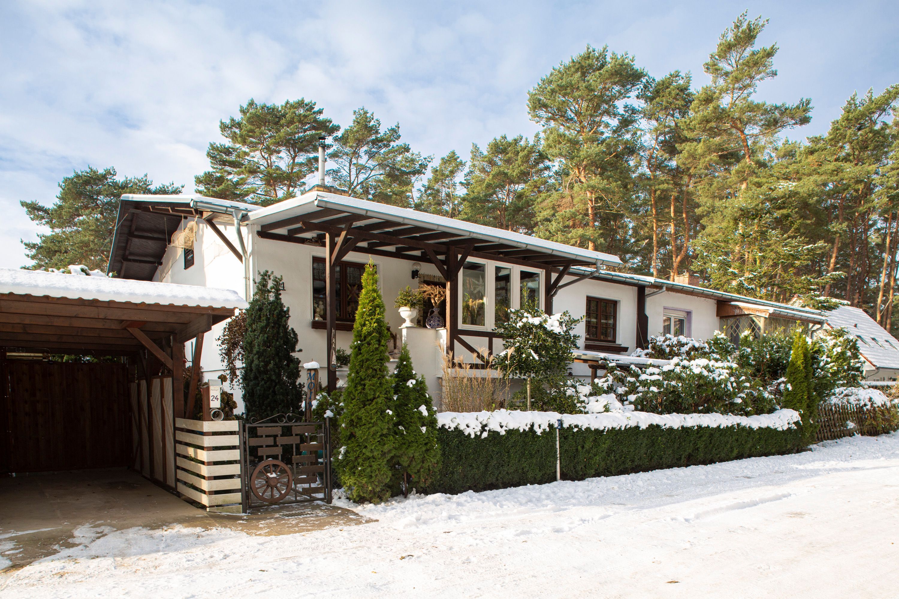 Una casa de dos pisos con un camino cubierto, valla de madera y terreno cubierto de nieve.
