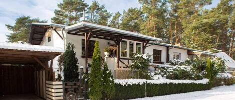Una casa de dos pisos con un camino cubierto, valla de madera y terreno cubierto de nieve.