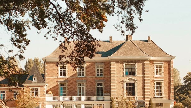 A large, multi-story brick building with a symmetrical facade, a central entrance with a portico, and a reflection in the water in front. - Maison Mairie (Hasselt)