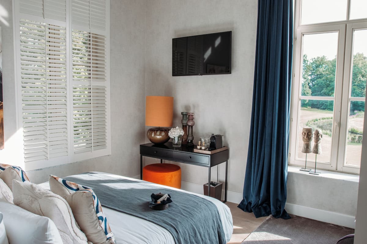 A bedroom with a bed, a desk with a lamp, and a window with curtains.