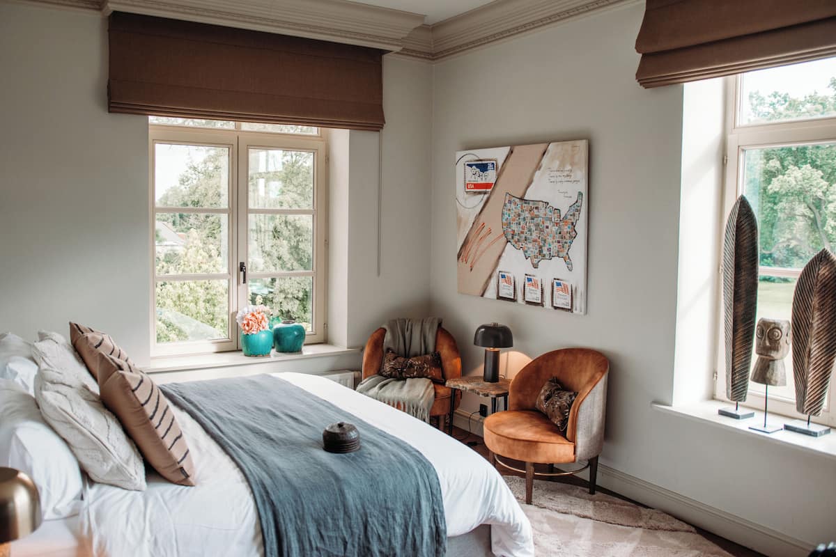 A bedroom with a large bed, a desk, and a chair. There is a window with a view of trees and a map on the wall.