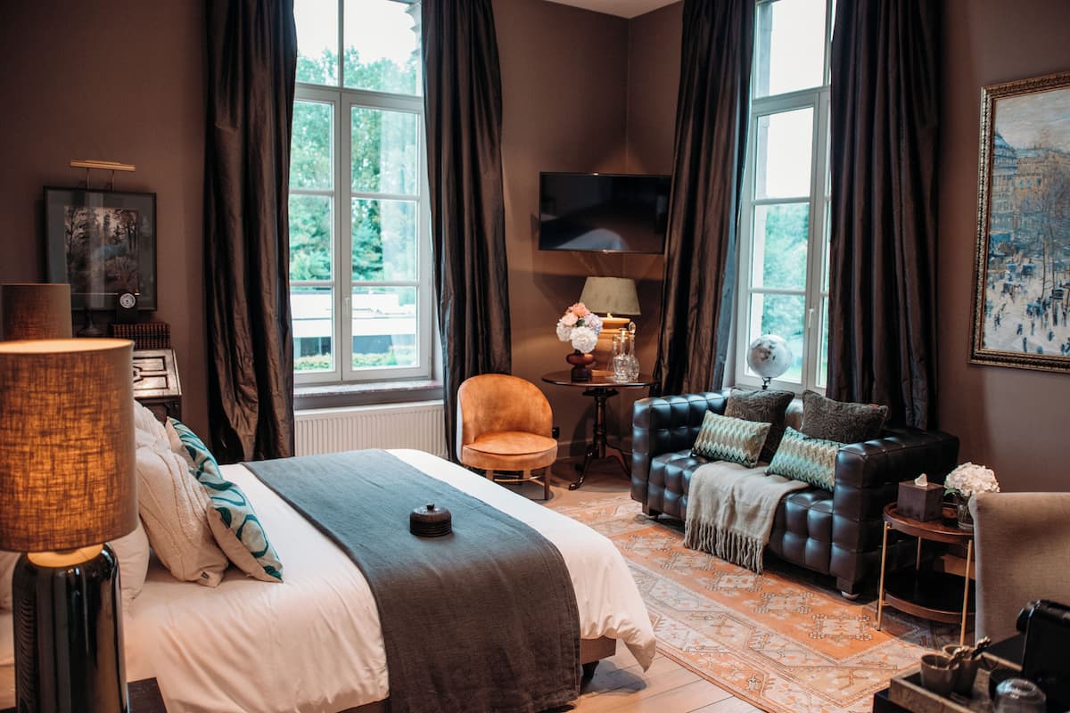 A hotel room with a bed, a sofa, a TV, and a window with curtains.
