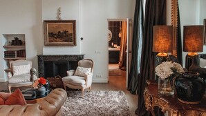 A living room with a fireplace, a sofa, a coffee table, and a chair. There is a painting on the wall and a vase with flowers on a side table. - Maison Mairie (Hasselt)