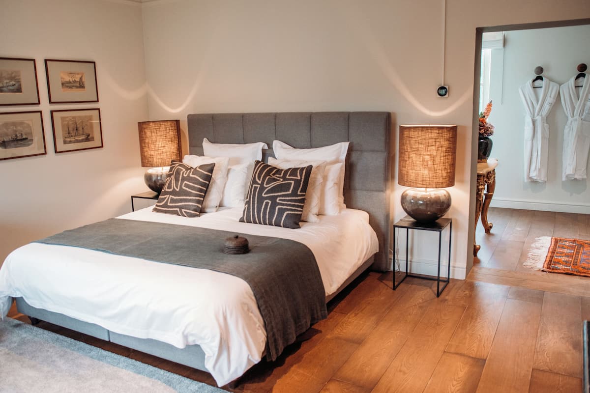 A neatly arranged bedroom with a large bed, bedside lamps, and framed pictures on the wall.