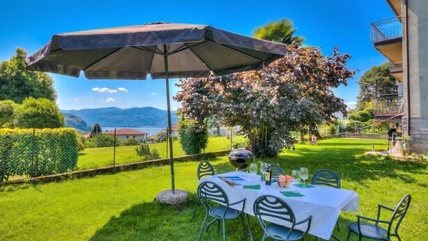 A table set outdoors with an umbrella, surrounded by greenery and a view of mountains. - Residenza Il Parco - Family Retreat With Garden (Ispra)