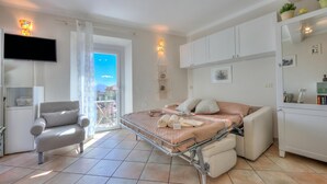 Un dormitorio moderno con cama, una silla, televisor y balcón con vistas.