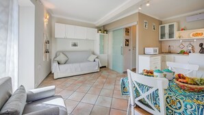 Una cocina moderna con armarios blancos, un comedor con mesa para dos y una sala de estar con sofá y televisor.