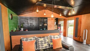 Un salon moderne avec un canapé en cuir noir, une tête de lit en bois et un mur recouvert de carreaux verts.